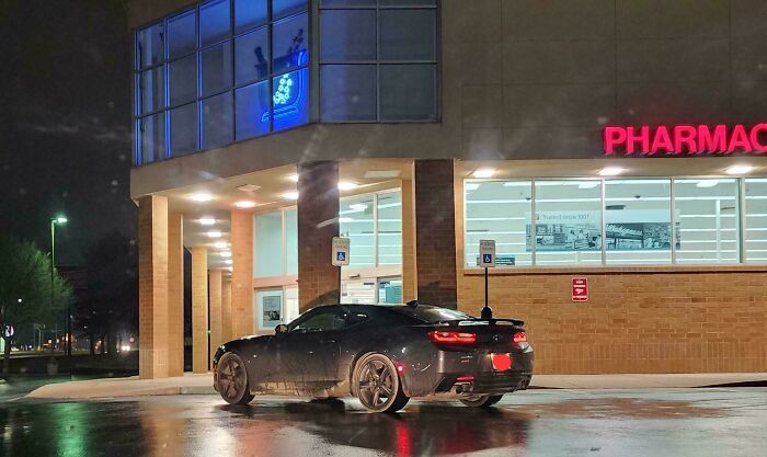 An entitled person's dark grey car parked illegally in a handicap spot in front of a pharmacy at night.