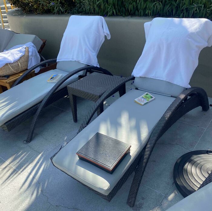 Two entitled pool lounge chairs are reserved with towels and personal items, implying occupants are away.