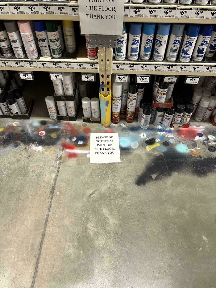 A sign on the floor of a hardware store asks people not to spray paint the floor, surrounded by entitled spray paint.