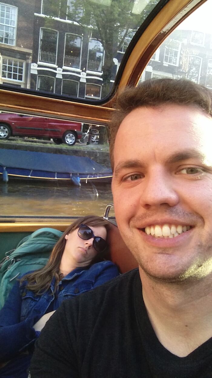A smiling man takes a selfie with a woman sleeping next to him on a boat, showcasing trips that didn't go as planned.