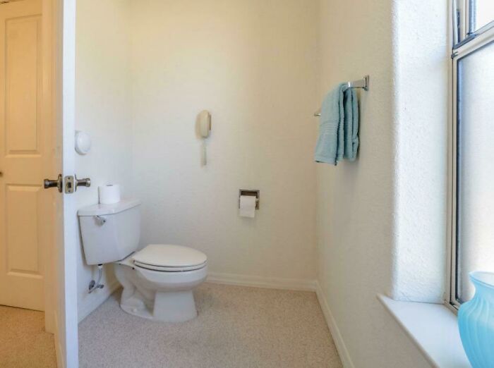 A toilet in a bathroom with a telephone on the wall, a funny design fail.