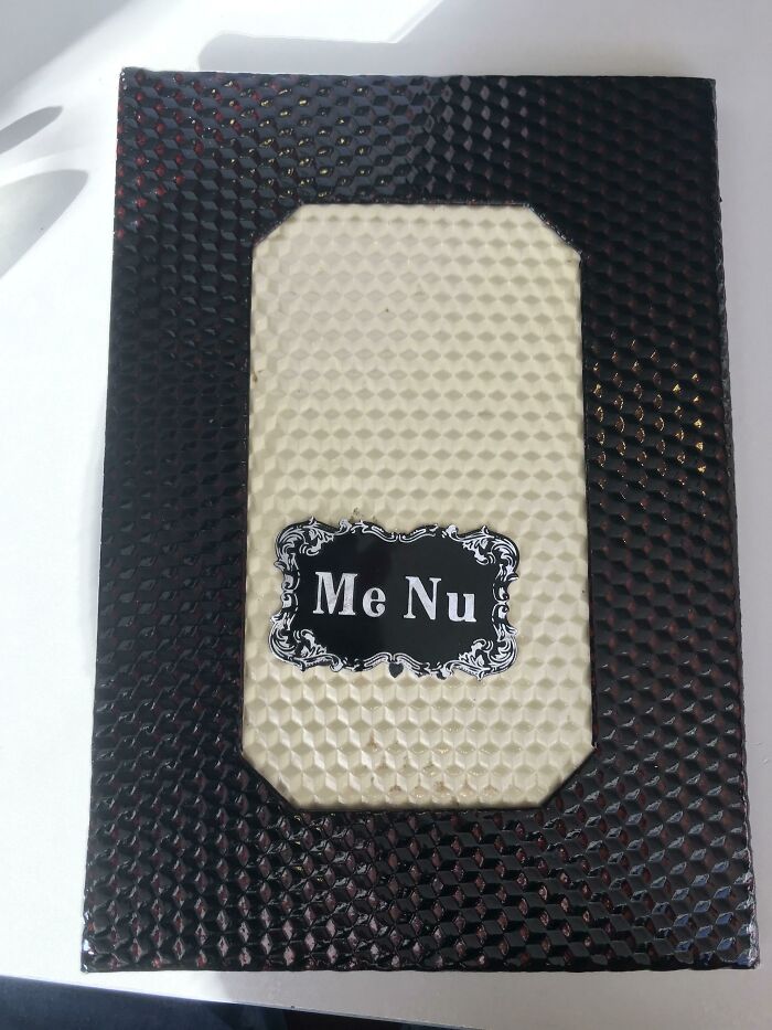 A close-up of a restaurant menu cover with 'Me Nu' spelled out, highlighting a hilarious design fail.