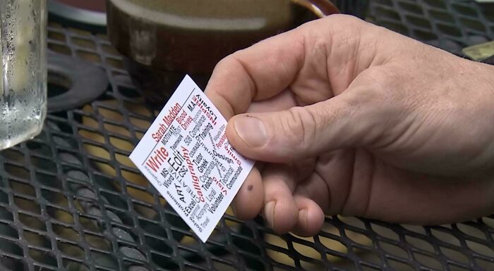 A hand holding a small card with densely packed text, an impressive design fail in its readability.