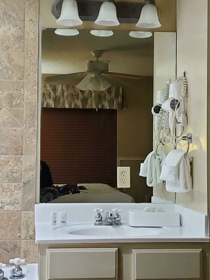 A bathroom mirror reflecting a bedroom with a ceiling fan, a common design fail in hotel room layouts.