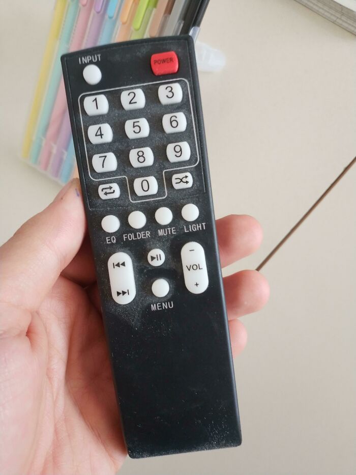 A hand holding a remote control with two play/pause buttons, highlighting an impressive design fail.