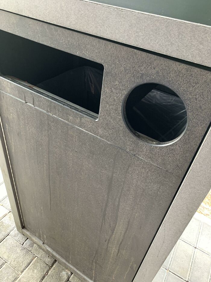 A dark gray recycling bin with a rectangular opening and a circular opening, both for waste, a design fail.