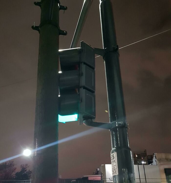 Traffic light showing a green arrow pointing left on a dark street, an impressive design fail.