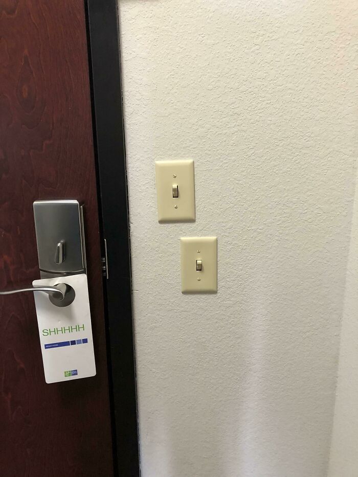 Two light switches placed unevenly on a wall next to a wooden door with a 'SHHHH' sign, a clear design fail.