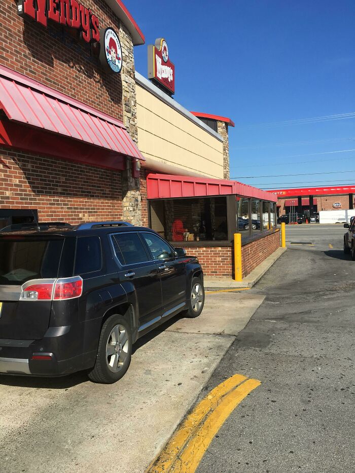 A black SUV parked awkwardly close to a Wendy's drive-thru window, highlighting a design fail in parking lot layout.