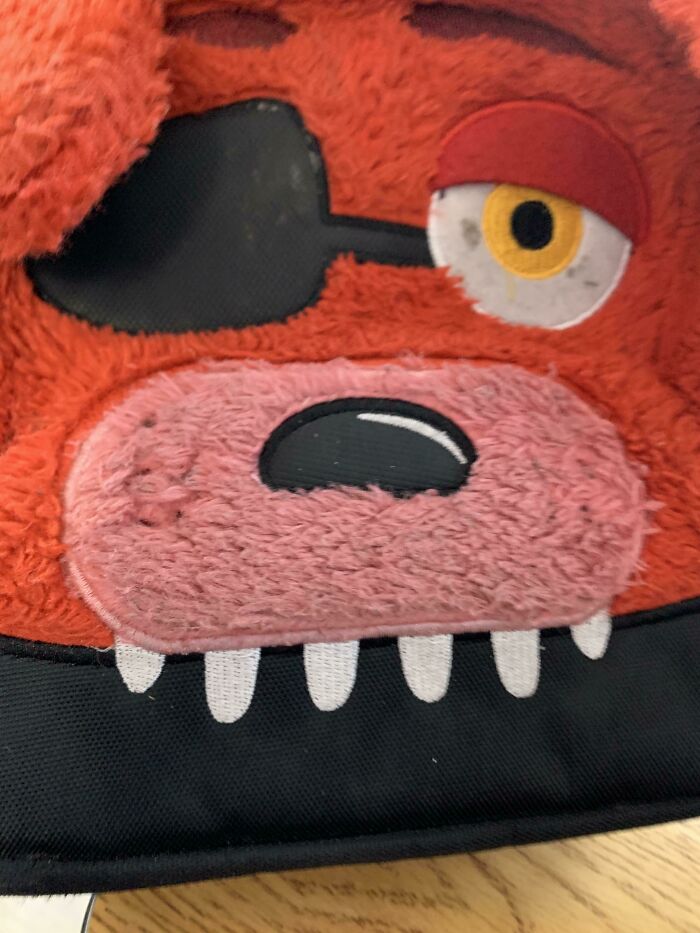 A close-up of a red, furry character plush with an eye patch and large design fails mouth.