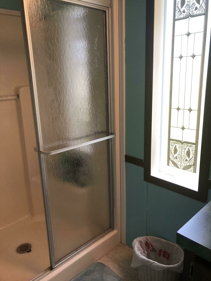 A shower stall next to a window with stained glass design fails, in a bathroom with blue walls.