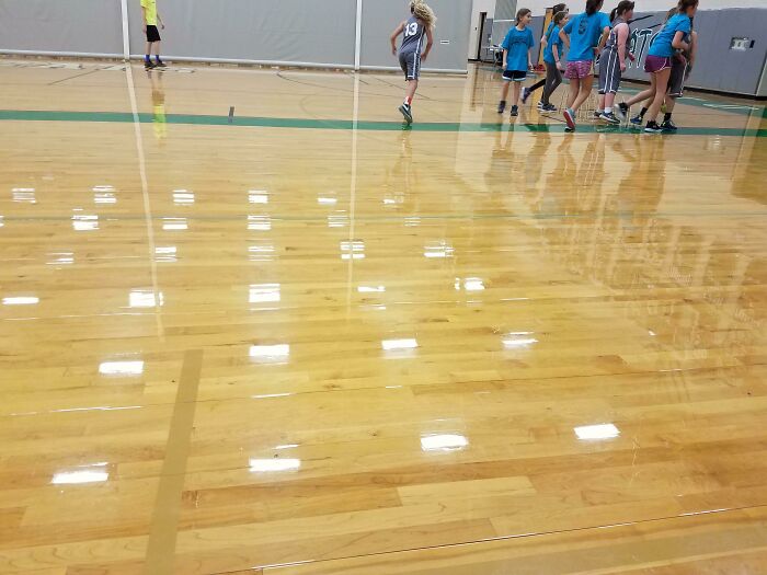 Children playing on a glossy gym floor that reflects the ceiling lights, showcasing an interesting design aspect.