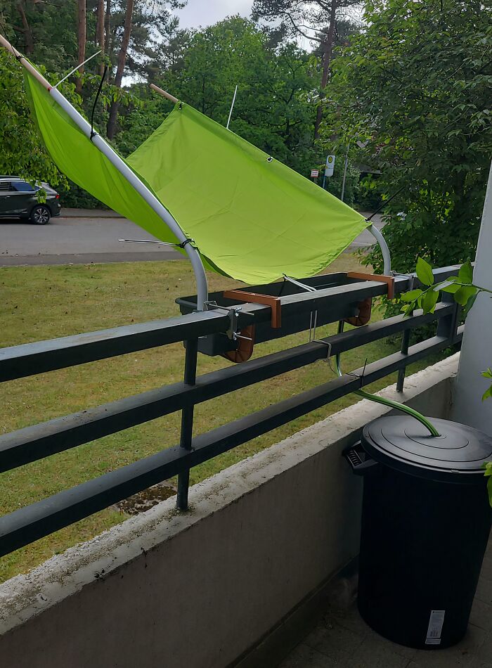 A bright green fabric sunshade rigged over a balcony railing, a clever solution for outdoor comfort.