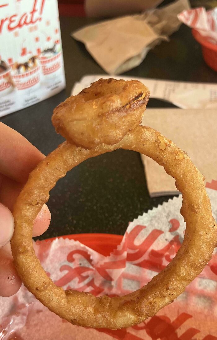 A hand holds a fried onion ring shaped like a diamond ring, a weird moment that made the day interesting.