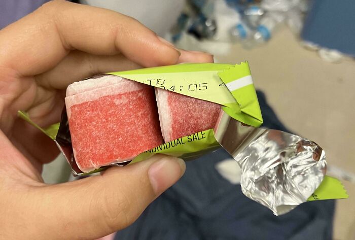 A hand holds an opened package of red candy, revealing unexpected moments inside.