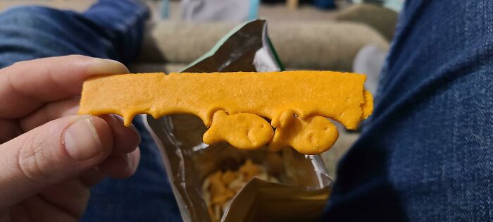 A person holding an unusually long goldfish cracker, an unexpected moment that made their day more interesting.