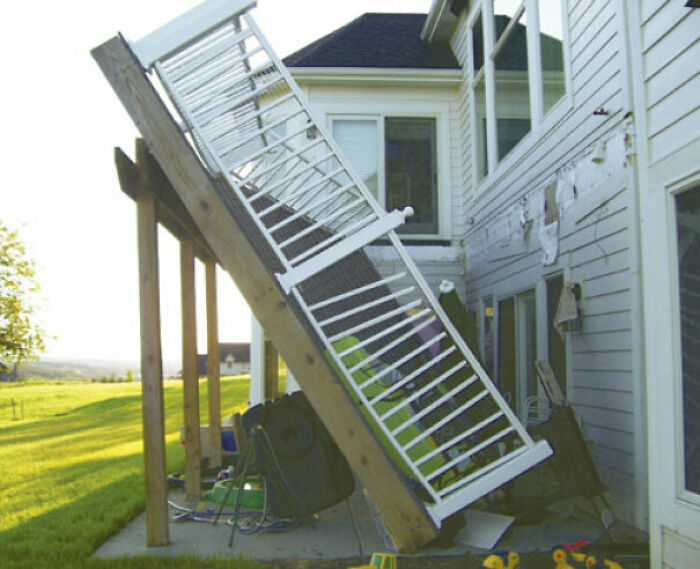 A hilariously bad DIY example of a collapsed deck with a fence falling off a house.