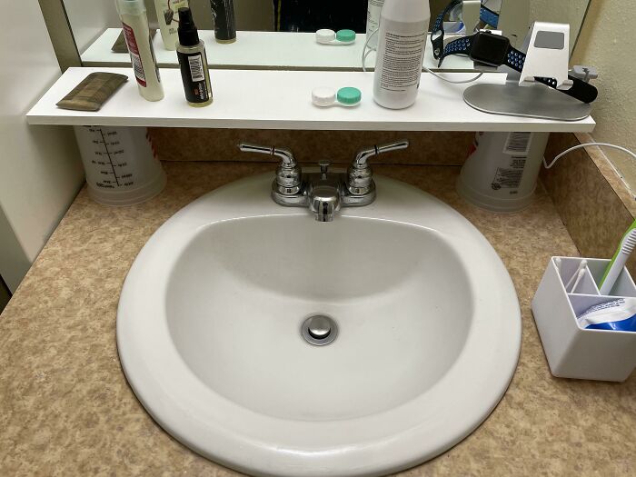 Hilariously bad DIY example: a makeshift bathroom shelf supported by measuring cups above a sink.