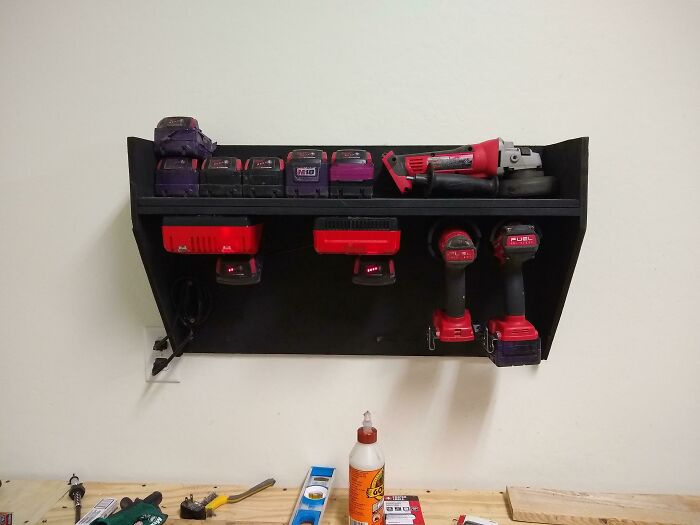 Hilariously bad DIY example: a collection of power tools and chargers stored on a wall-mounted shelf.