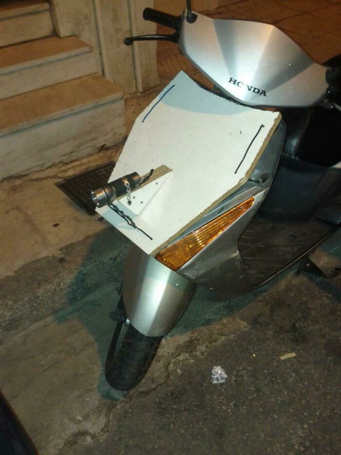 Hilariously bad DIY example: A scooter with a makeshift white panel and a flashlight strapped to its front.