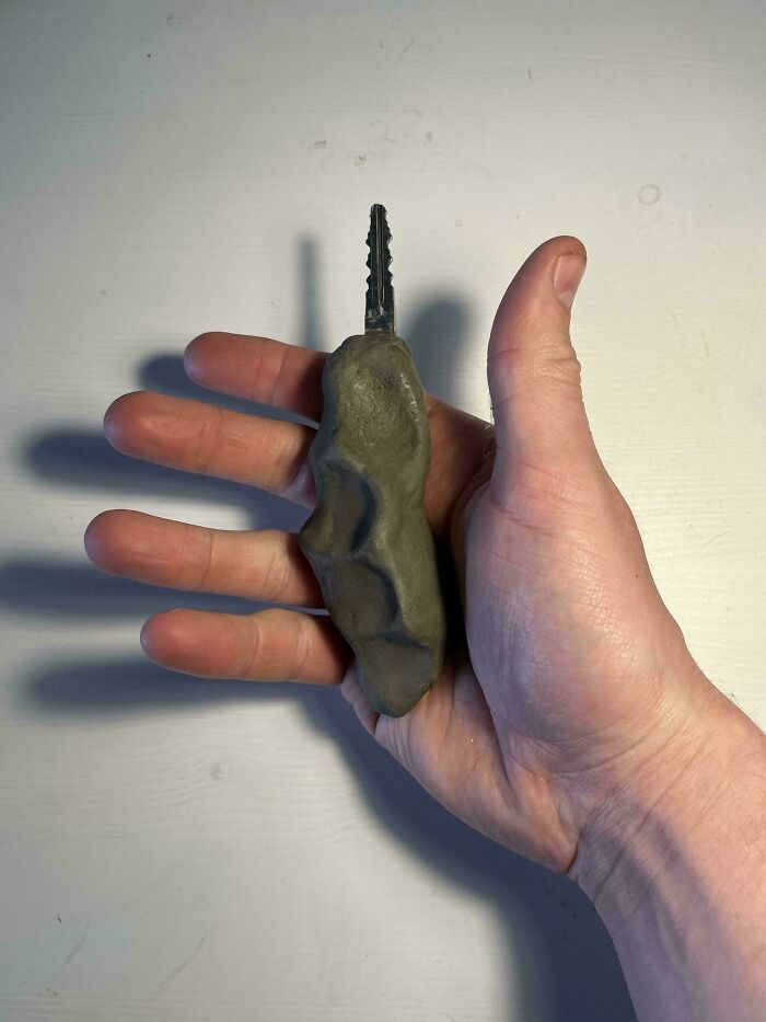A hand holding a key with a custom, oddly shaped clay handle, an interesting and unique design choice.