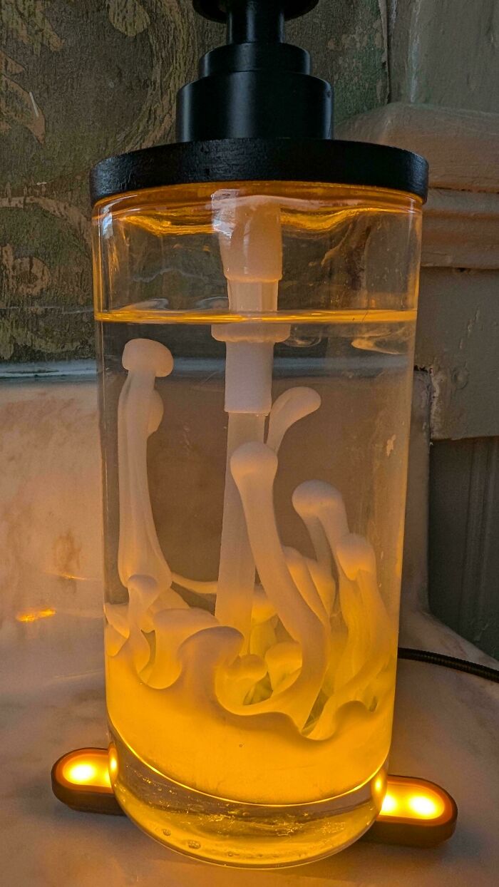 A clear bottle with a black pump, filled with liquid, glowing yellow, containing white bone-like shapes, a weird and interesting moment.