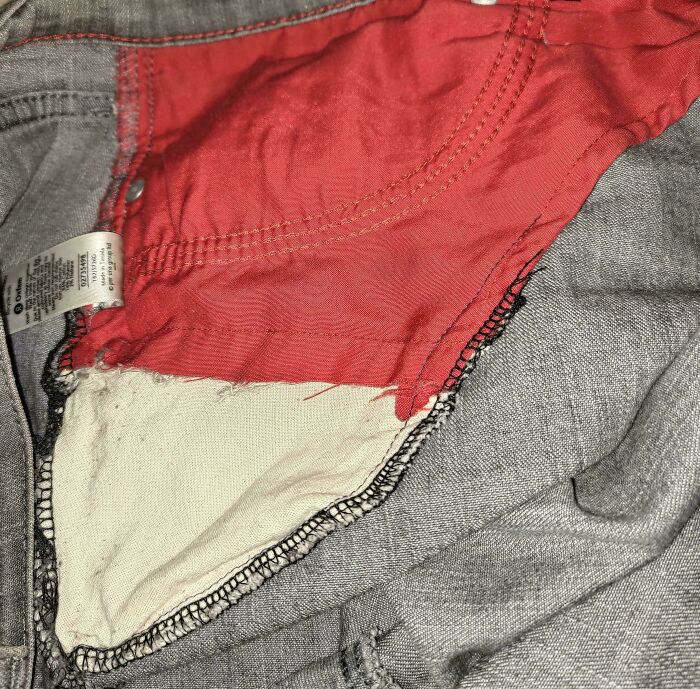 Close-up of gray jeans with a torn red and cream-colored inner pocket lining. A weird fashion moment.