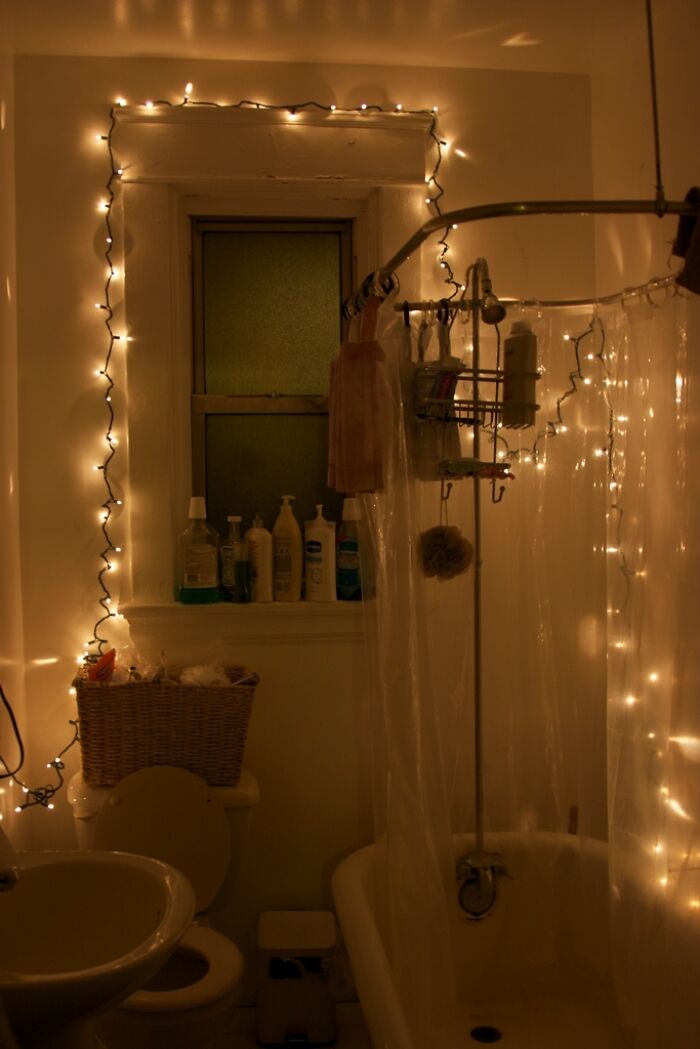 Hilariously bad DIY example: A bathroom poorly lit with numerous string lights around a window and shower.