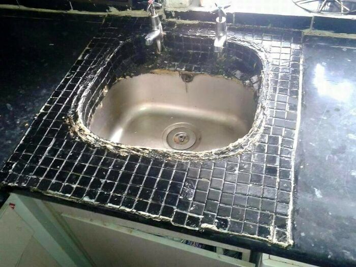 A hilariously bad DIY example: a kitchen sink with poorly installed, black mosaic tiles around its edge.