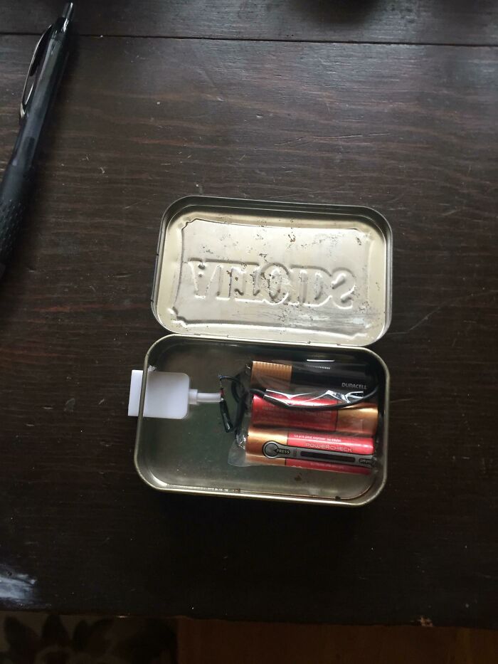 A hilariously bad DIY portable charger crafted from batteries inside a metal Altoids tin with a charging cable.