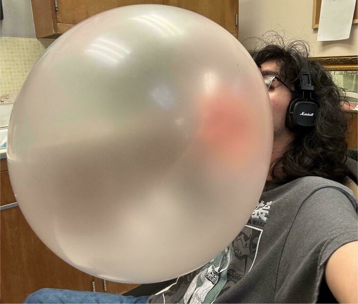 A person with headphones on blowing a gigantic bubblegum bubble that obscures most of their face, a weird moment.