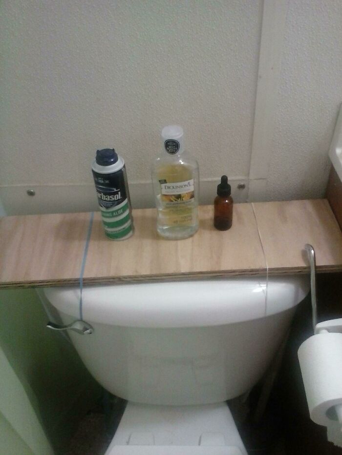 A hilariously bad DIY shelf made from a wooden board and string resting on a toilet with toiletries.