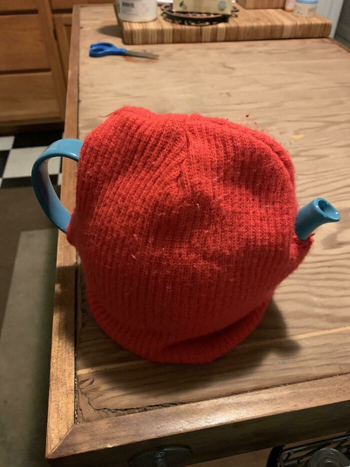 A bad example of DIY home decor: a teapot covered with a red knitted hat.