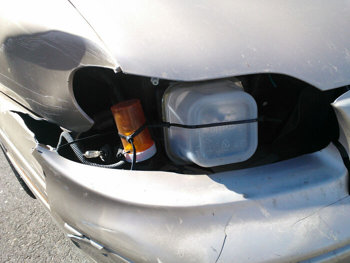 Hilariously bad DIY car repair with a plastic container and an orange light for a headlight.