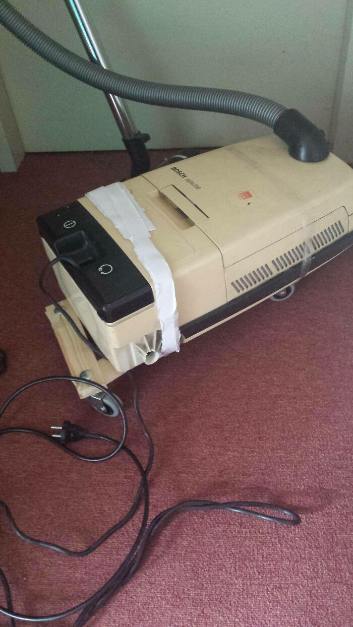 Hilariously bad DIY vacuum cleaner repair, with a wooden base taped to the bottom of the old vacuum.