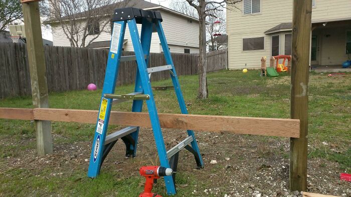Hilariously bad DIY construction with a ladder supporting a wooden beam between two posts.