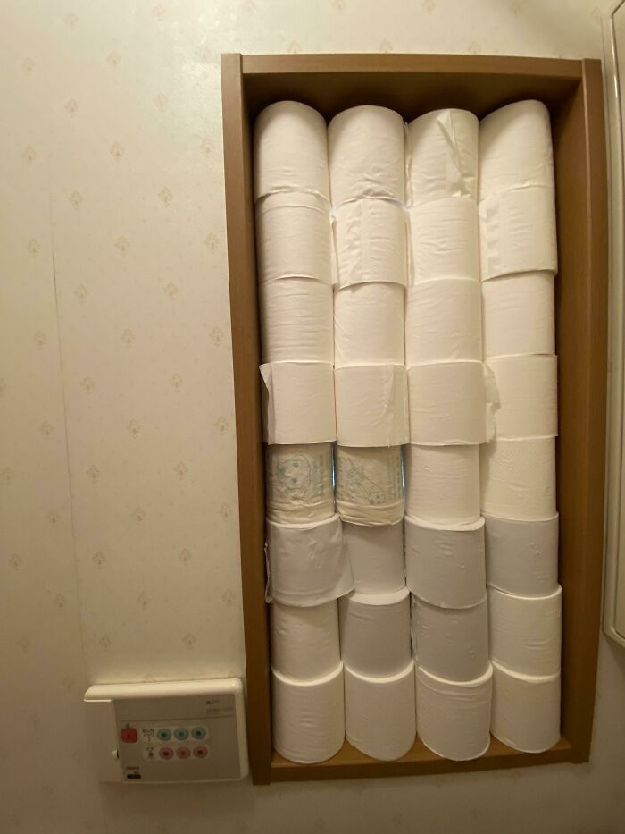 Hilariously bad DIY toilet paper storage in a narrow wooden shelf filled with rolls.