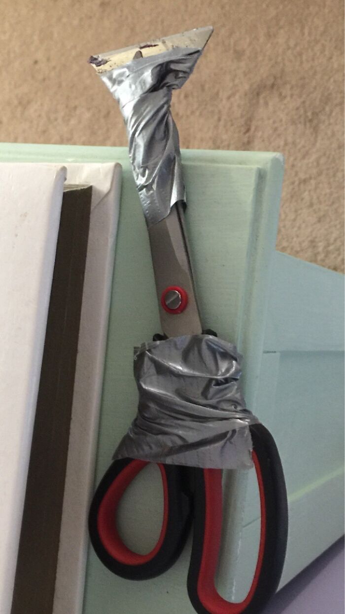 A pair of scissors with a utility blade taped to one end, a hilariously bad example of DIY.