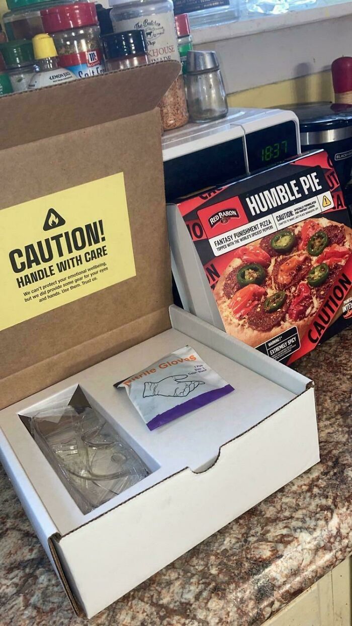 A box labeled 'CAUTION! HANDLE WITH CARE' containing gloves and safety glasses, next to a pizza box, a weird moment.