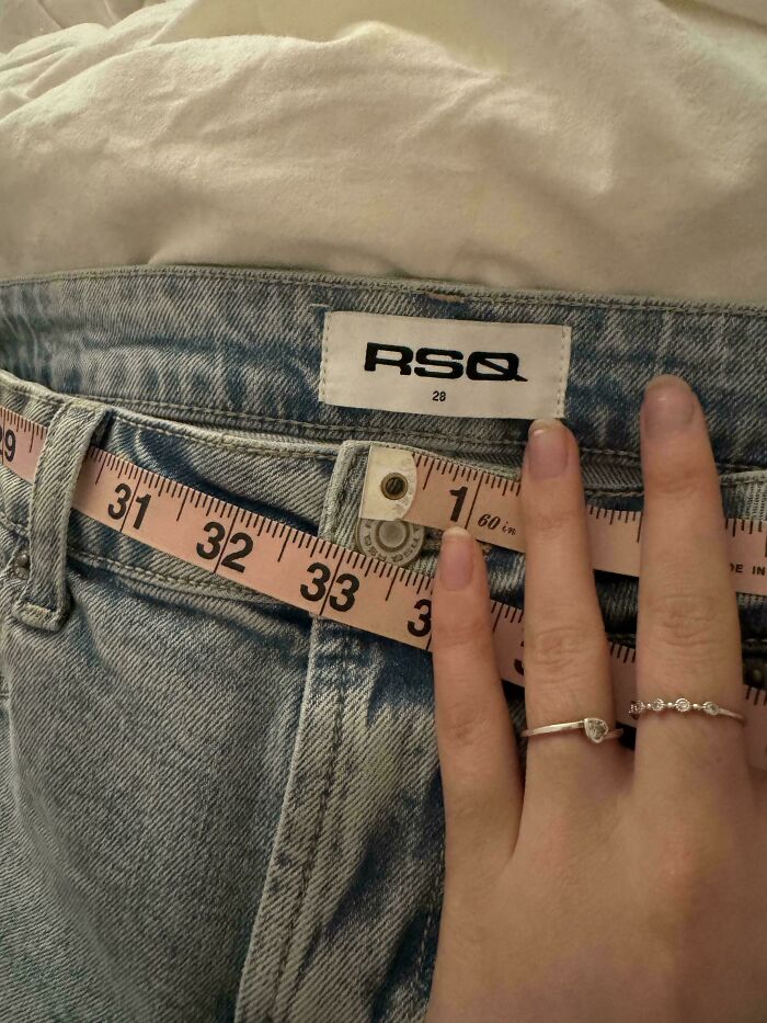 A person holding a measuring tape against a pair of RSQ brand jeans, a weird moment that made the day interesting.