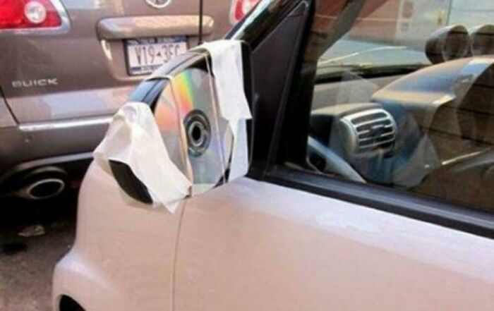 A hilariously bad DIY car repair: a CD taped to a car's side mirror as a makeshift replacement.