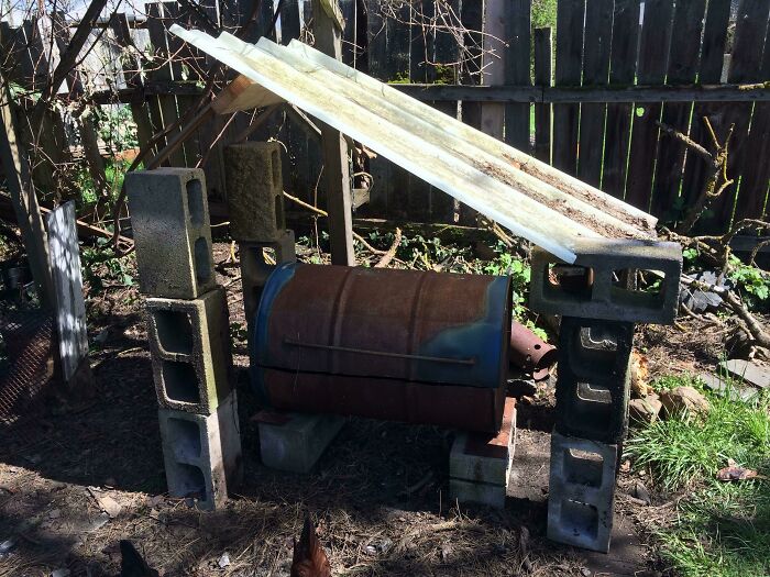 Hilariously bad DIY barbecue smoker built from a rusted barrel and cinder blocks with a makeshift roof.