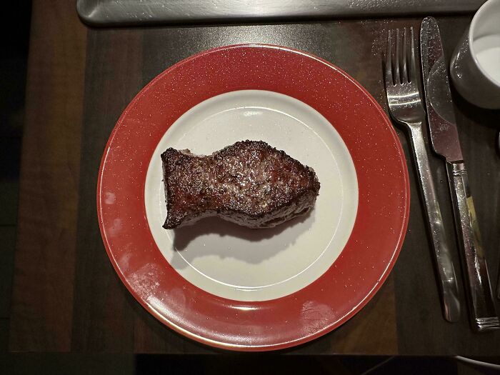 A grilled steak on a white and red plate with cutlery, an unexpected moment that made the day interesting.