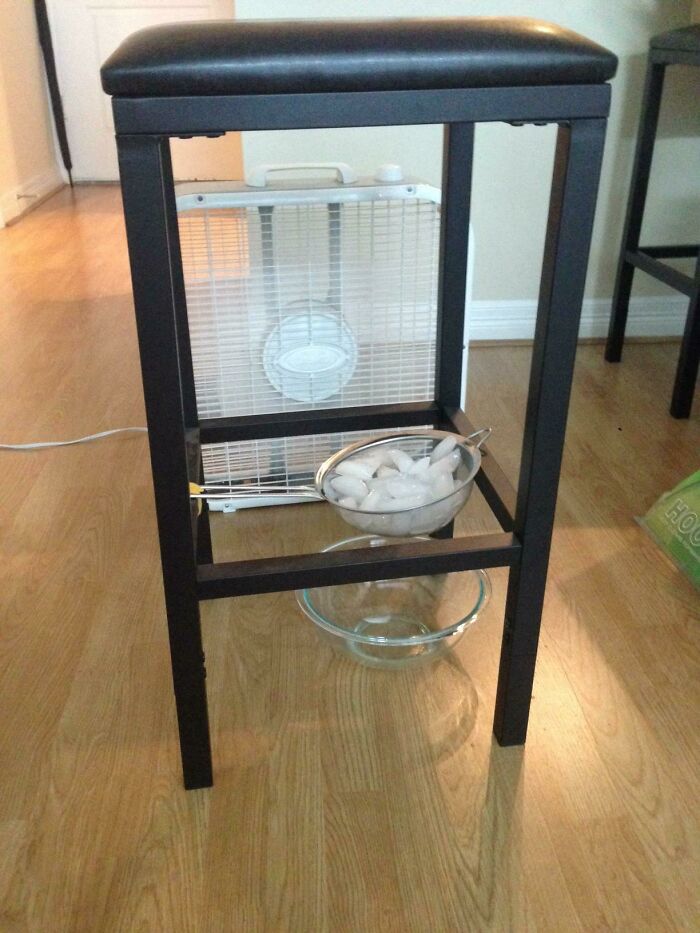 A fan and bowls of ice beneath a stool, attempting to cool a room, a hilariously bad example of DIY