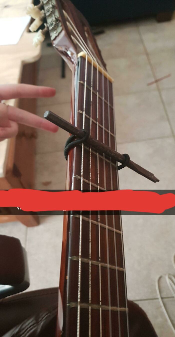 A guitar fretboard with a pencil and rubber band acting as a capo, a hilariously bad example of DIY