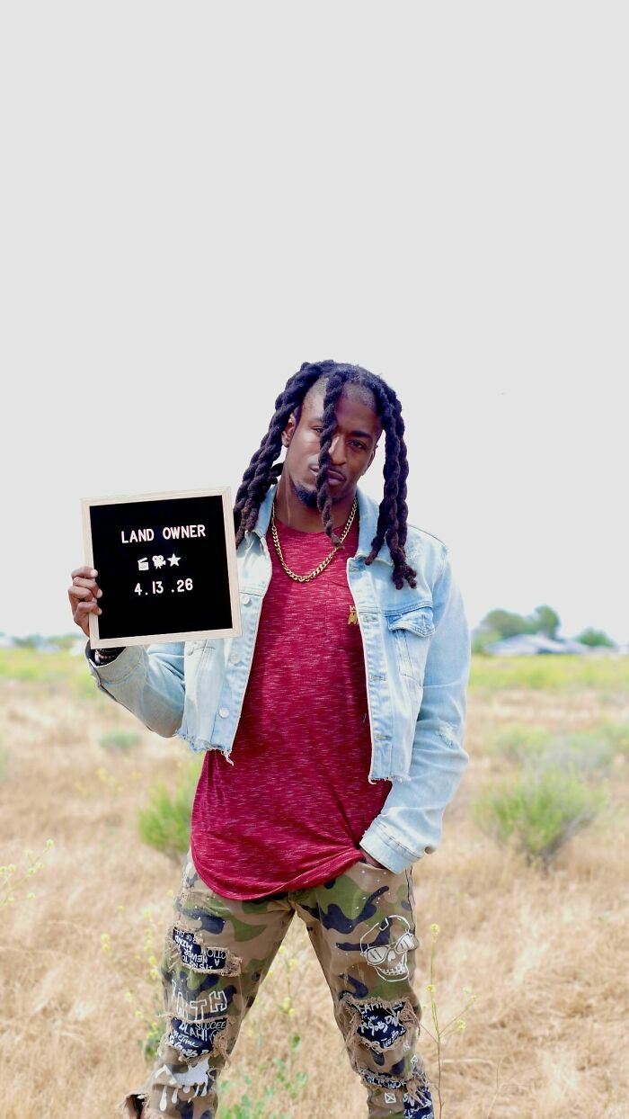 Man with dreadlocks holding a 'LAND OWNER' sign, celebrating an incredible accomplishment