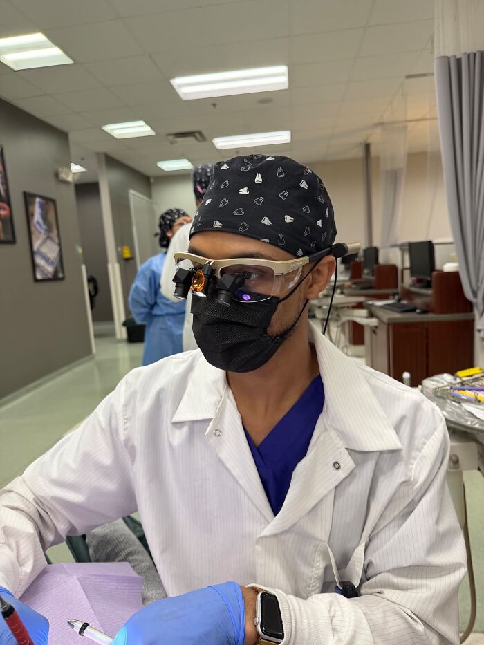 A dentist in a cap and mask, wearing magnifying glasses, working on a patient, representing incredible accomplishments.