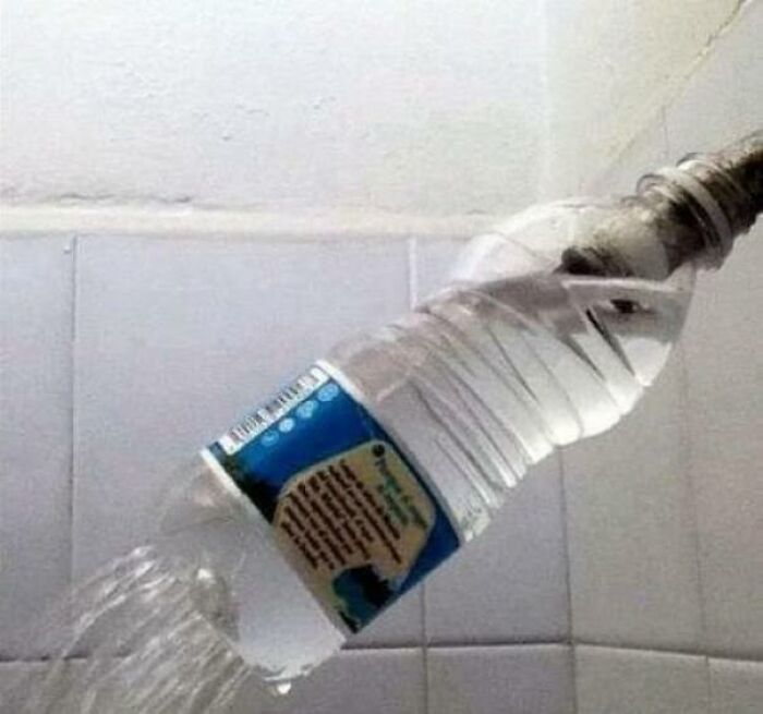 A hilariously bad DIY shower head made from a plastic water bottle attached to a pipe, with water spraying out.