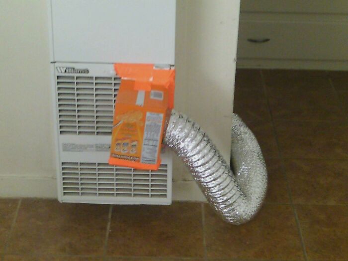 A hilariously bad DIY fix: a flexible silver duct hose taped to an air conditioner unit with an orange bag.