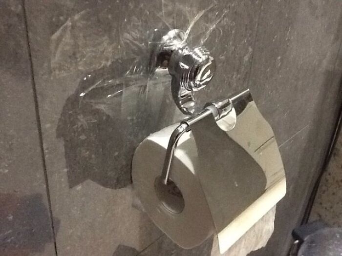 A hilariously bad DIY toilet paper holder with plastic wrap covering the wall fixture, indicating a leak.